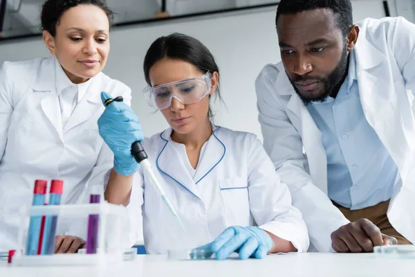 African american scientists standing near colleague with pipette and test tubes — Stock Photo