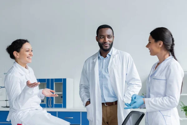 Sorridenti medici multietnici in camici bianchi che parlano in clinica — Foto stock