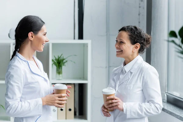 Doctor with paper cup talking to african american colleague — Stock Photo