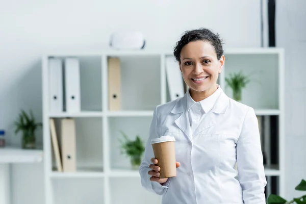 Smiling african american doctor holding paper cup in clinic — Stock Photo