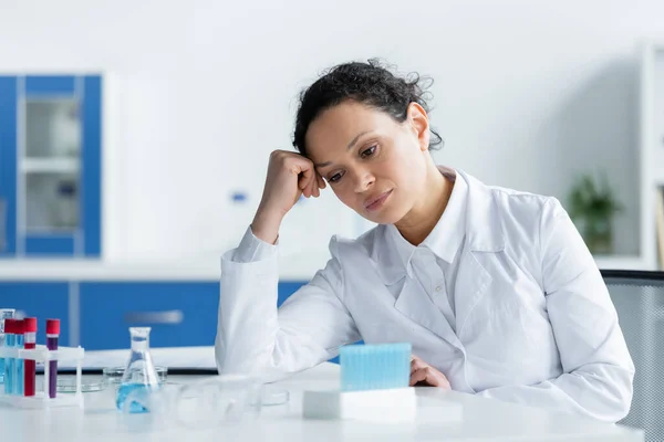 Cientista afro-americano exausto olhando para equipamentos médicos desfocados em laboratório — Fotografia de Stock