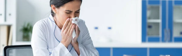 Doctor in white coat sneezing in clinic, banner — Stock Photo