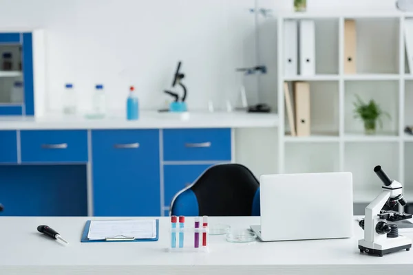 Laptop near microscope and test tubes in lab - foto de stock