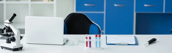 Test tubes and petri dishes near microscope and laptop in laboratory, banner — Stock Photo