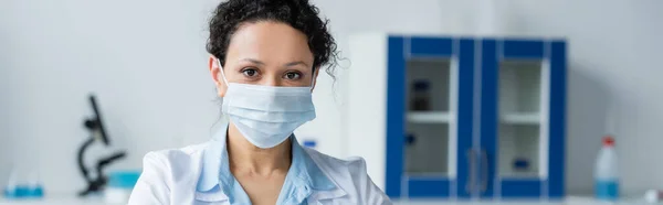 African american doctor in medical mask looking at camera in hospital, banner — Stock Photo