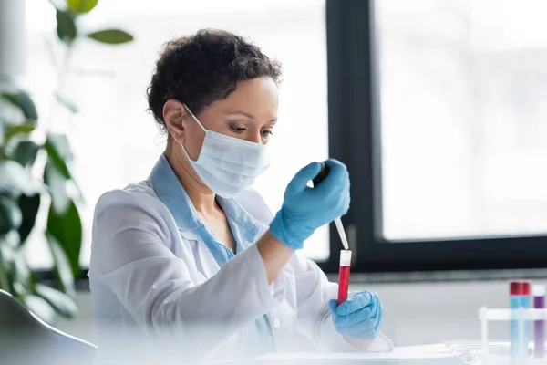 African american scientist in medical mask making experiment with equipment in lab — Stock Photo