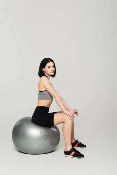 Sportswoman with vitiligo sitting on fitness ball on grey background — Stock Photo