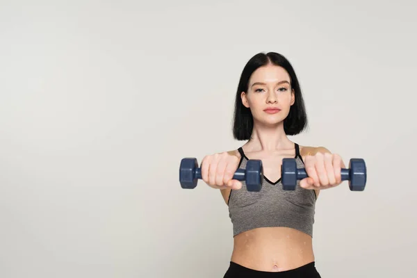 Sportswoman with vitiligo exercising with blurred dumbbells isolated on grey — Stock Photo