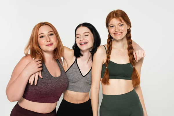 Smiling sportswoman with vitiligo embracing friends isolated on grey — Stock Photo