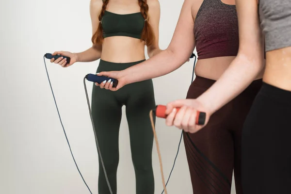 Cropped view of body positive sportswomen holding jump ropes isolated on grey — Stock Photo