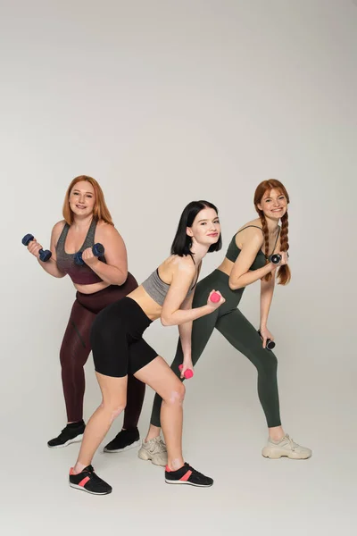 Femmes corps positif faisant de l'exercice avec haltères sur fond gris — Photo de stock