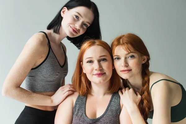 Young body positive sportswomen hugging isolated on grey — Stock Photo