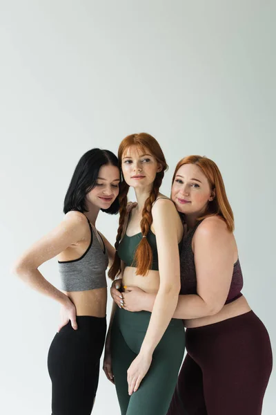 Plus size sportswoman embracing freckled friend isolated on grey — Stock Photo