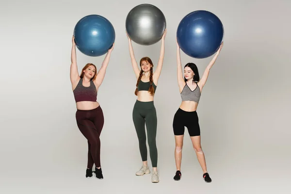 Körperlich positive Sportlerinnen mit Fitnessbällen auf grauem Hintergrund — Stockfoto