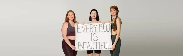 Body positive sportswomen holding placard with every body in beautiful isolated on grey, banner — Stock Photo