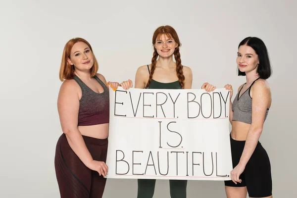 Corps souriant sportif positif femme tenant une pancarte avec tous les corps en beau lettrage isolé sur gris — Photo de stock