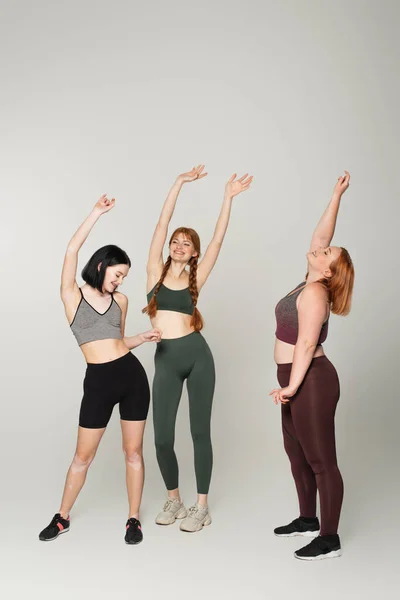 Jóvenes deportistas cuerpo positivo bailando sobre fondo gris - foto de stock