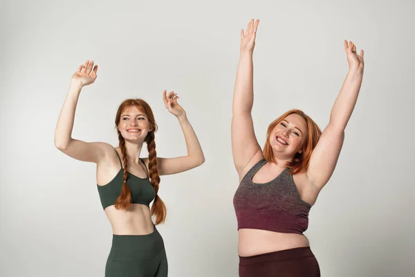 Corpo sorridente esportistas positivos levantando as mãos isoladas no cinza — Fotografia de Stock