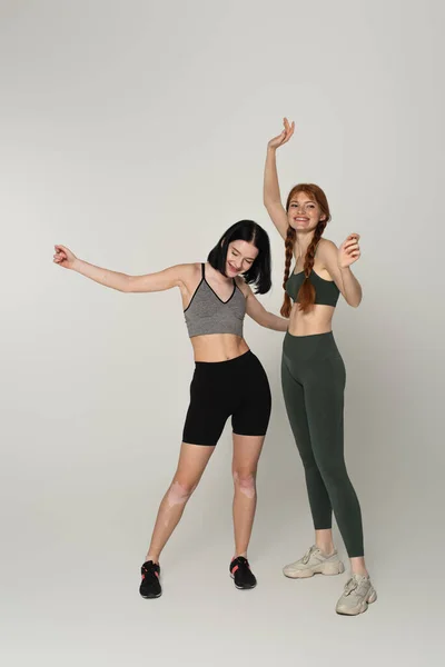Cheerful young sportswomen with vitiligo and freckles dancing together on grey background — Stock Photo
