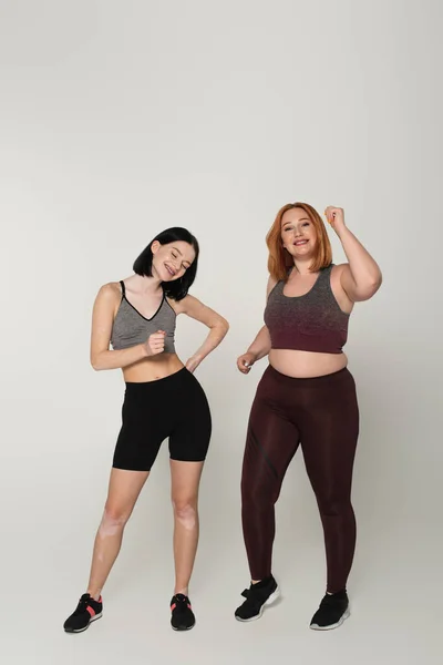 Body positive friends in sportswear dancing on grey background — Stock Photo