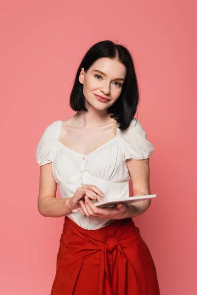 Mulher sorridente com vitiligo segurando tablet digital isolado em rosa — Fotografia de Stock