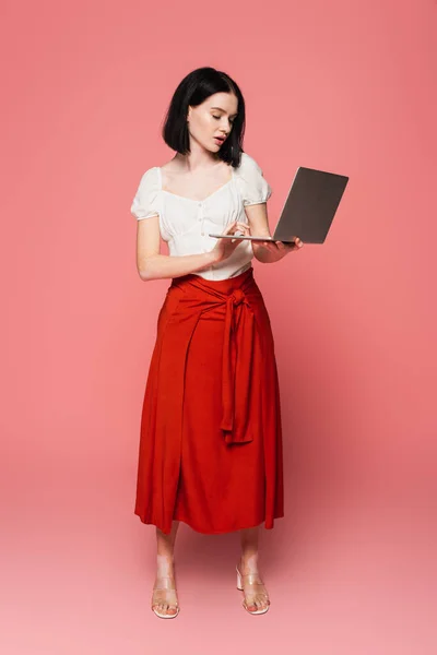 Stylish woman with vitiligo holding laptop on pink background — Stock Photo