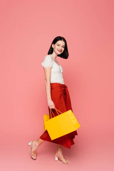 Pretty woman with vitiligo holding shopping bags while walking on pink background — Stock Photo