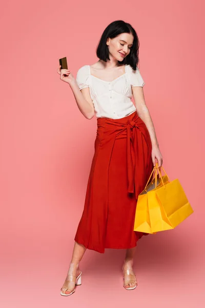 Mujer feliz con vitiligo sosteniendo bolsas de compras y tarjeta de crédito sobre fondo rosa - foto de stock