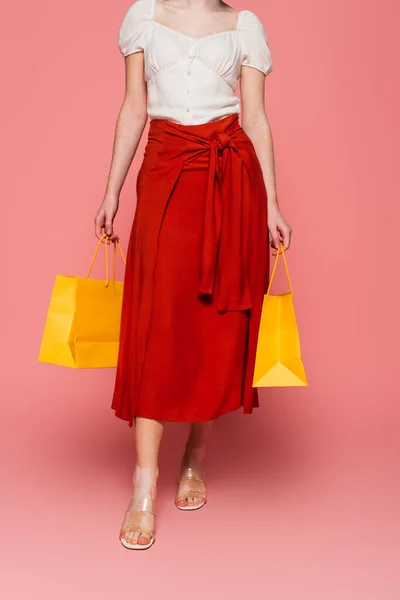 Vista recortada de la mujer elegante con vitiligo sosteniendo bolsas de compras sobre fondo rosa - foto de stock