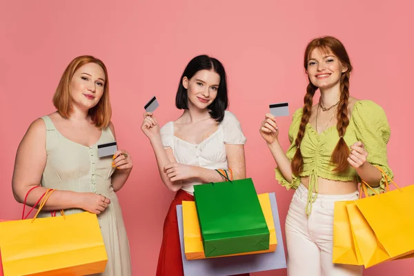 Corps des femmes positives avec des cartes de crédit et des sacs à provisions isolés sur rose — Photo de stock