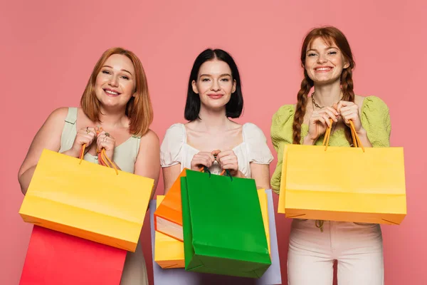 Mulher sorridente com vitiligo segurando sacos de compras perto do corpo amigos positivos no fundo rosa — Fotografia de Stock