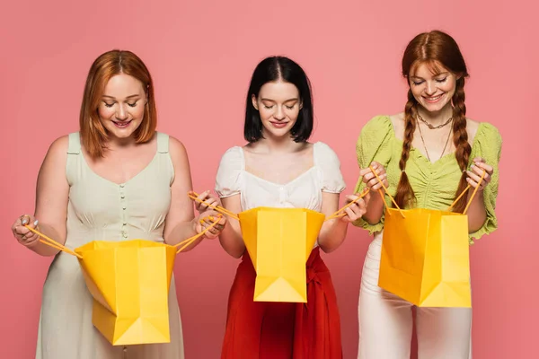 Corps des femmes positives regardant sacs à provisions isolés sur rose — Photo de stock