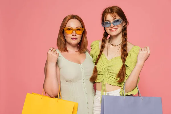 Stylische Körper positive Freunde in Sonnenbrille mit Einkaufstaschen isoliert auf rosa — Stockfoto