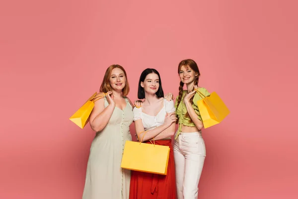 Young body positive women with shopping bags hugging isolated on pink — Stock Photo