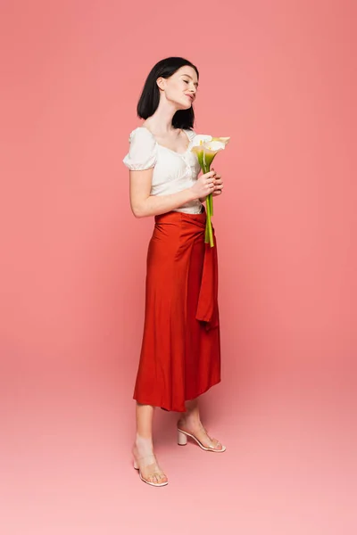 Mujer elegante con vitiligo sosteniendo lirios de cala sobre fondo rosa - foto de stock