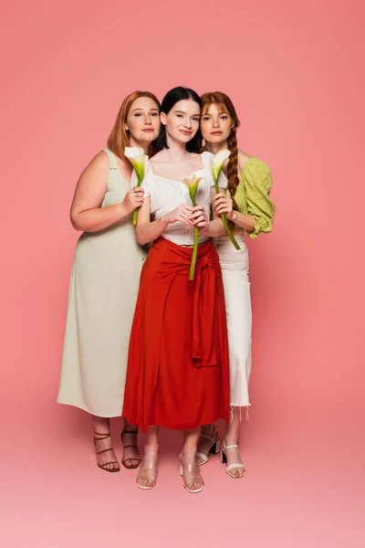 Body positive friends holding calla lilies on pink background — Stock Photo