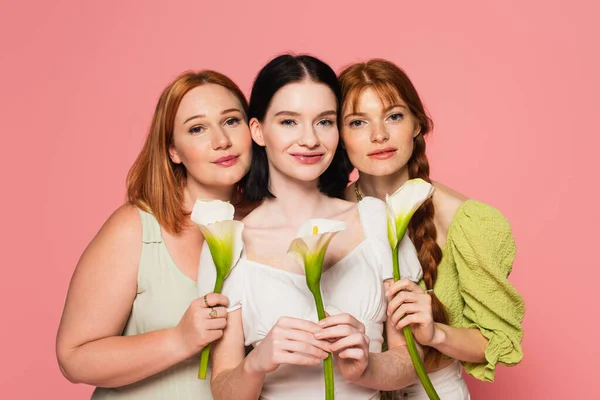 Mujer con vitiligo sosteniendo lirio calla cerca de amigos aislados en rosa - foto de stock