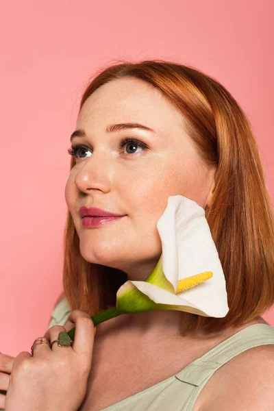 Mujer bonita sosteniendo lirio calla cerca de la cara aislado en rosa - foto de stock