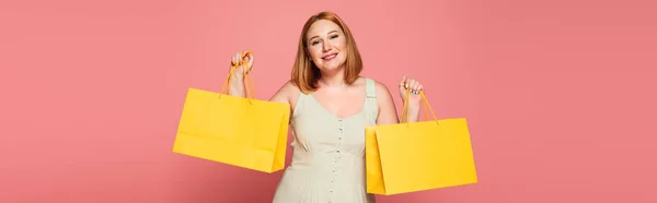 Smiling plus size woman holding shopping bags isolated on pink, banner — Stock Photo
