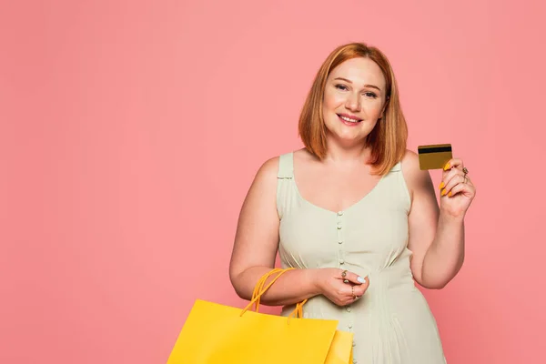 Mujer positiva de talla grande con tarjeta de crédito y bolsas aisladas en rosa - foto de stock