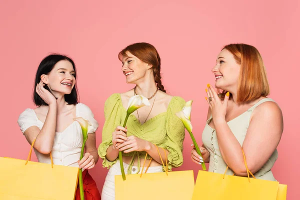 Corpo amigos positivos olhando para a mulher com vitiligo e saco de compras com flor isolada em rosa — Fotografia de Stock