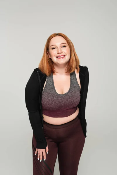 Happy body positive woman in sportswear looking at camera isolated on grey — Stock Photo