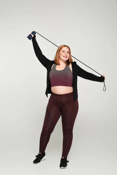 Lunghezza completa di più dimensioni sportswoman tenendo corda da salto su sfondo grigio — Foto stock