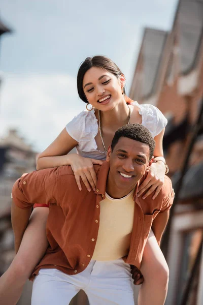 Happy african american man looking at camera while having fun with asian girlfriend — Stock Photo