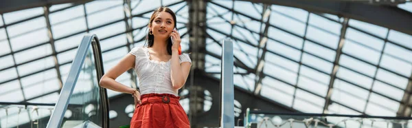 Bella donna asiatica con mano sul fianco chiamando sul telefono cellulare sulla scala mobile, banner — Foto stock