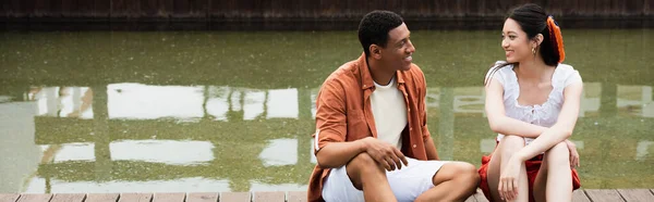 Jeune couple interracial souriant lors d'une conversation à la frontière près de l'eau, bannière — Photo de stock