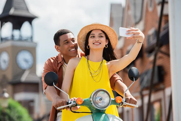 Feliz asiático mulher tomando selfie enquanto equitação scooter com africano americano homem — Fotografia de Stock