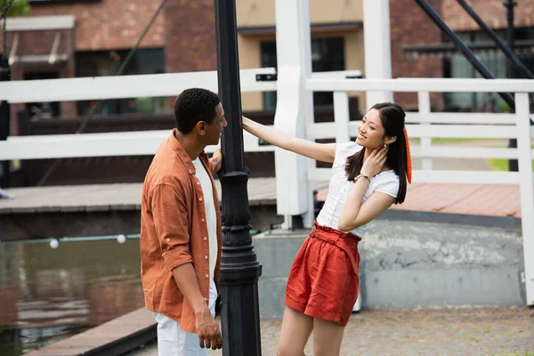 Happy asian woman looking at african american boyfriend during walk in icity — Stock Photo
