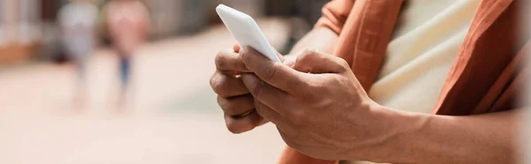 Vista parcial del hombre afroamericano mensajería en el teléfono celular al aire libre, pancarta — Stock Photo