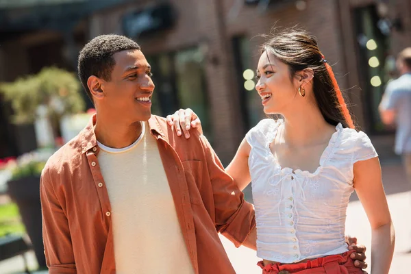 Alegre africano americano hombre abrazando bonito asiático mujer en urbano calle - foto de stock